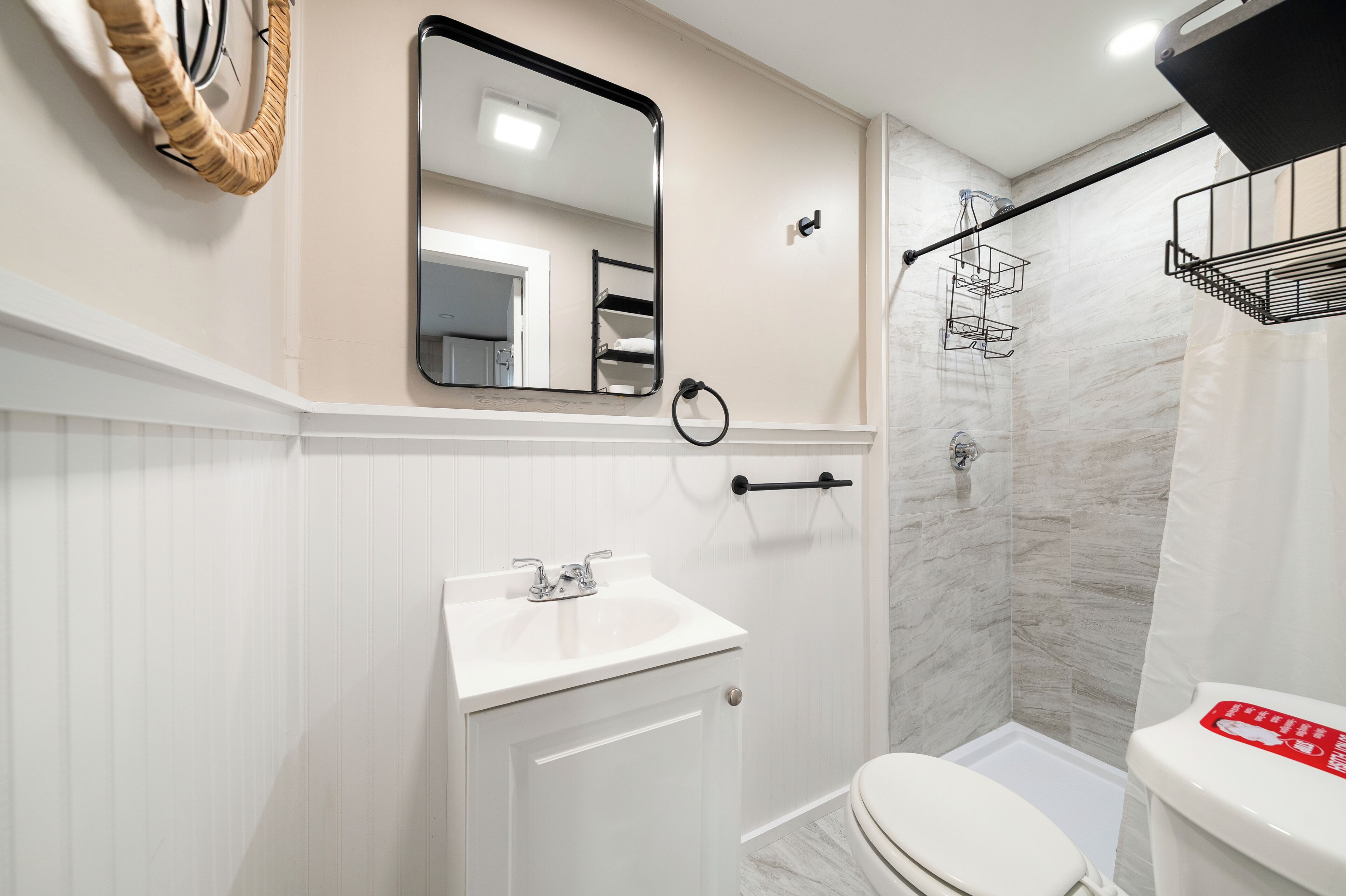 Een badkamer met een wit wastafel, toilet, douche en spiegel.