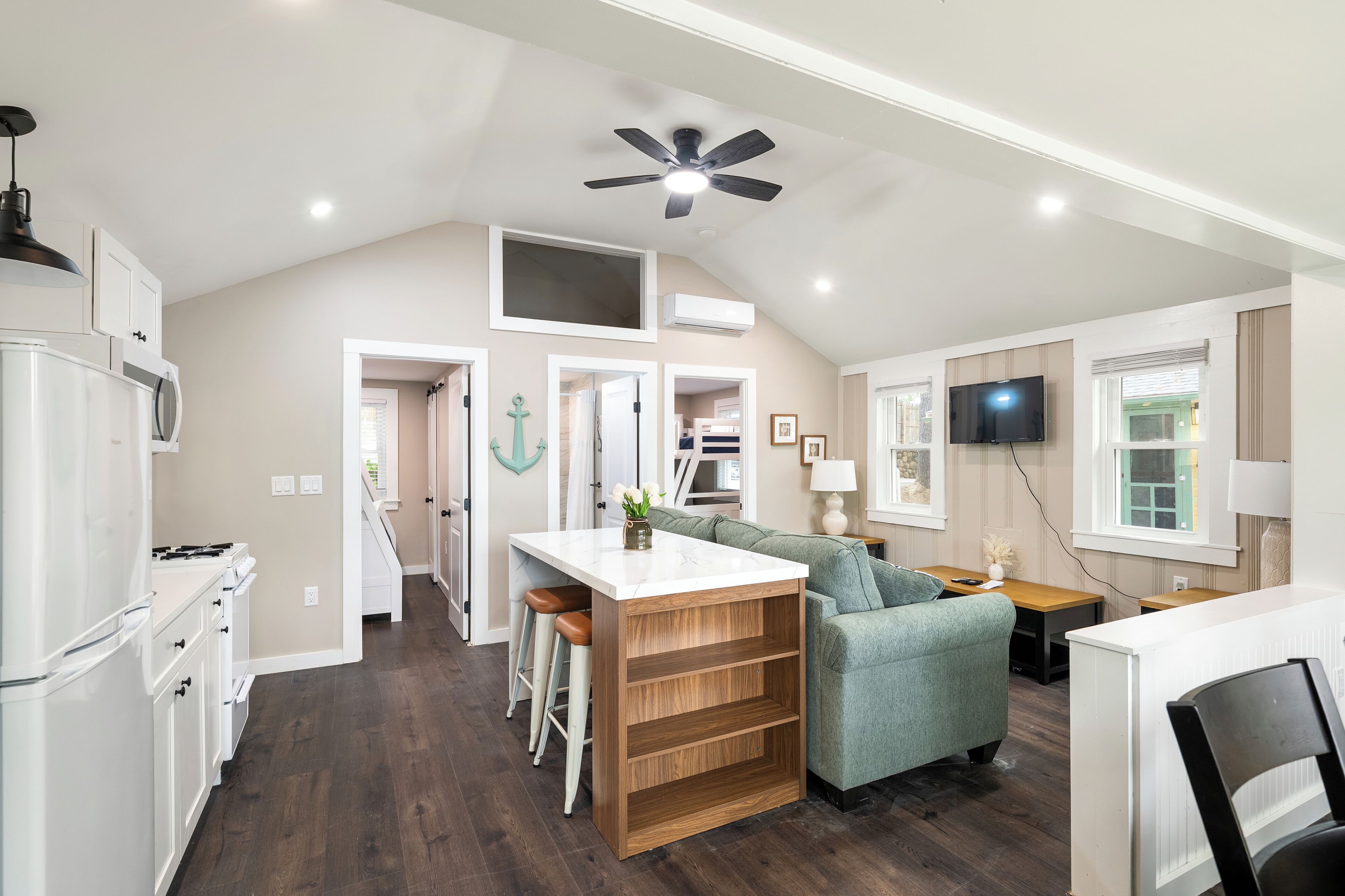A modern kitchen with a central island, a dining area with a green sofa, and a TV mounted on the wall.