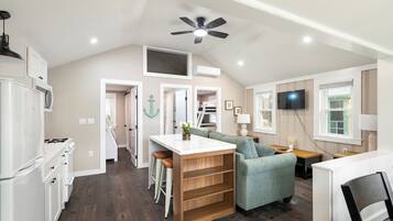 A modern kitchen with a central island, a dining area with a green sofa, and a TV mounted on the wall.