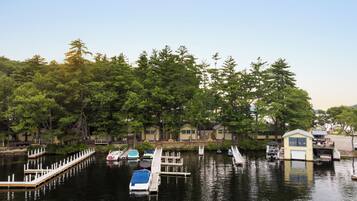Uma marina com barcos atracados, um pequeno barco atracado em primeiro plano e uma fileira de cabanas com uma floresta ao fundo.