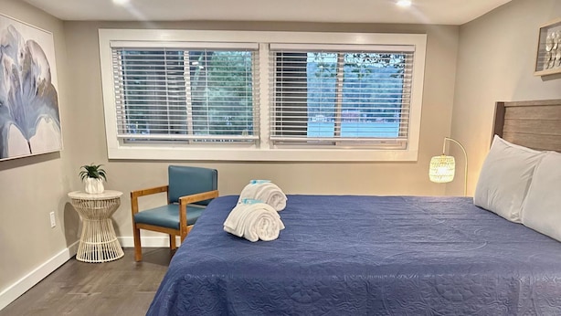 Ein Schlafzimmer mit einem großen Bett, einem Sessel, einem kleinen Tisch und einem Fenster mit Jalousien.