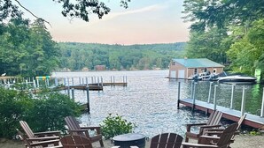 Eine Seeterrasse mit Adirondack-Stühlen, einem kleinen runden Tisch und Blick auf den See und anlegende Boote.