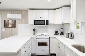 A modern kitchen with white cabinetry, a built-in microwave, a gas stove, and a coffee maker. - Cabin 16 at Historic Sandy Point Resort W/ Boat Slip and onsite boat ramp (Alton)