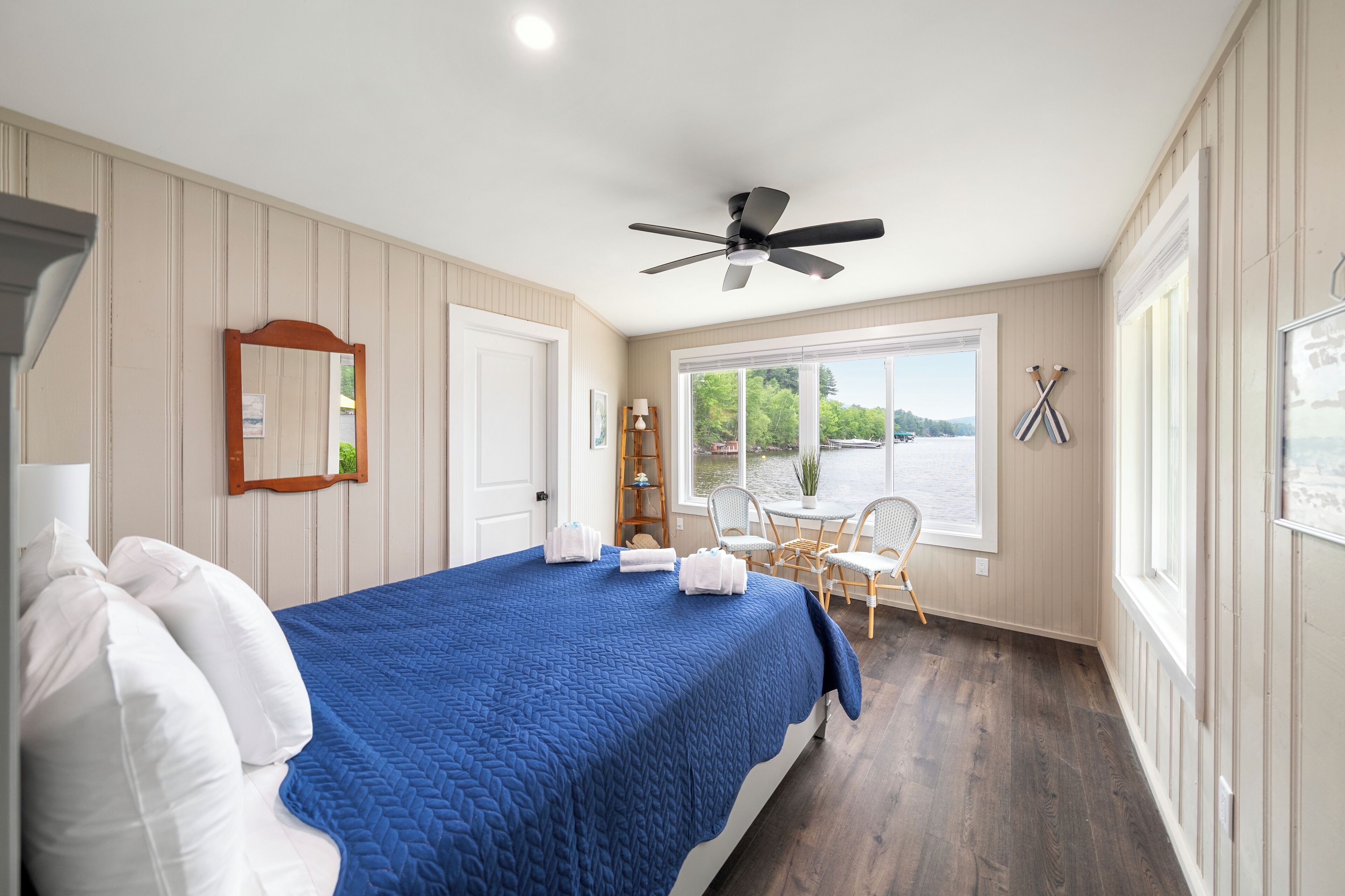 A bedroom with a bed, a ceiling fan, a window with a view of the outdoors, and a door.