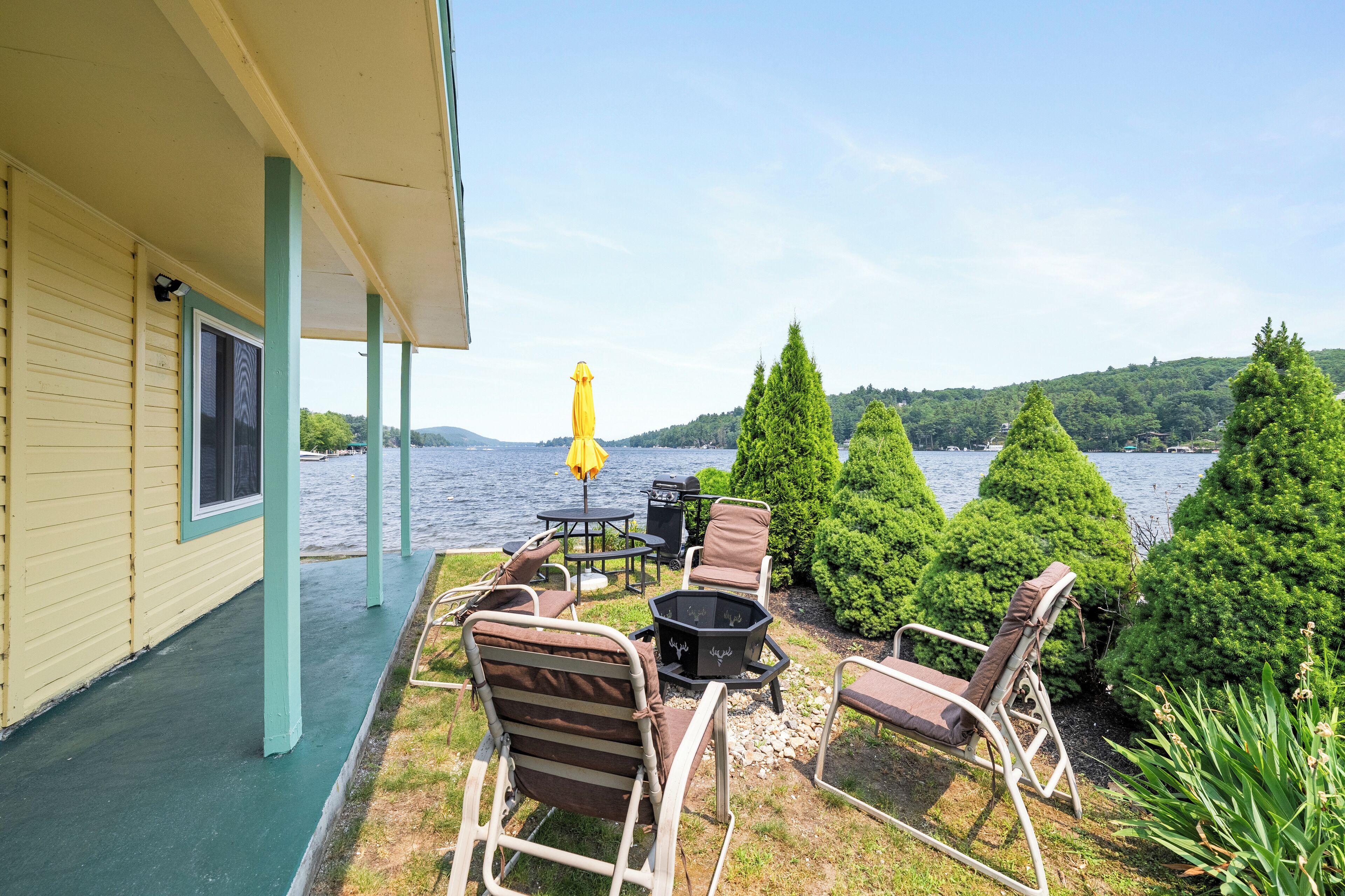 A covered patio with outdoor furniture, a fire pit, and a view of a lake and hills.