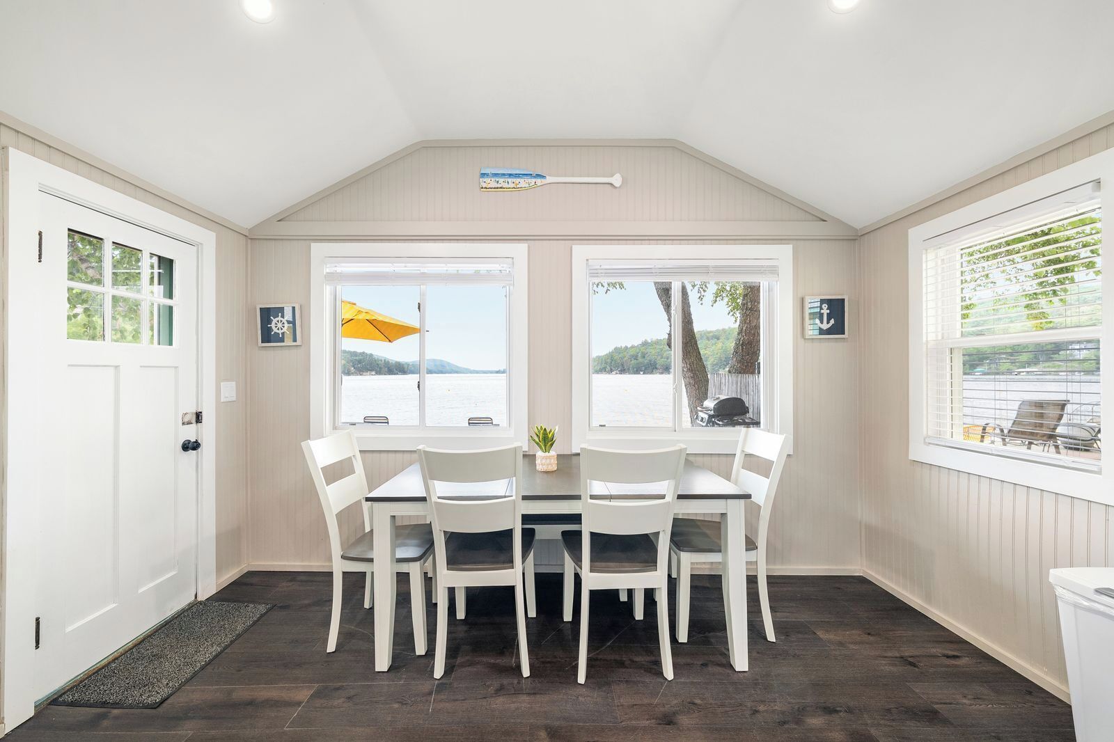 A dining area with a table and chairs, large windows with a view of the water, and a ceiling fan.