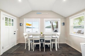 Un comedor con mesa y sillas, ventanas amplias con vista al agua y un ventilador de techo.