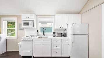 Una cocina con armarios blancos, estufa, microondas, fregadero y refrigerador.