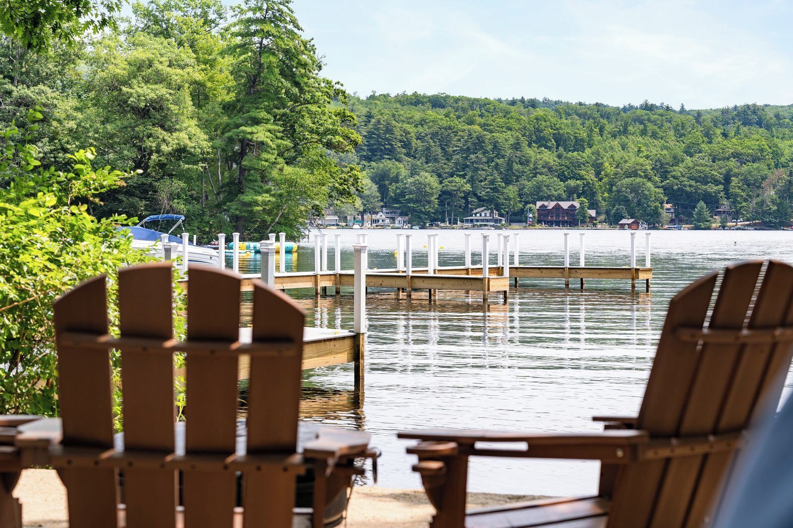 A lakeside view with wooden chairs and a dock extending into the water.