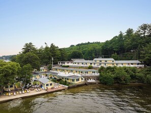 Um hotel à beira do rio com vários edifícios, um cais com espreguiçadeiras e uma encosta arborizada ao fundo.