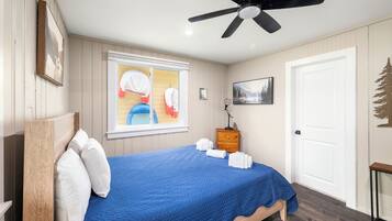 Un dormitorio con cama, ventilador de techo, ventana con persianas, mesita de noche y puerta.