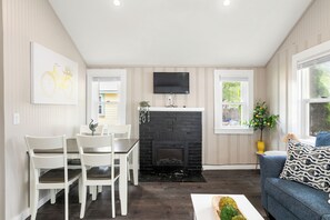 A modern living room with a fireplace, a dining area with white chairs, a flat-screen TV mounted above the fireplace, and a window with a view of greenery. - Cabin 60 at Historic Sandy Point Resort W/ Boat Slip and Onsite Boat Ramp (Alton)