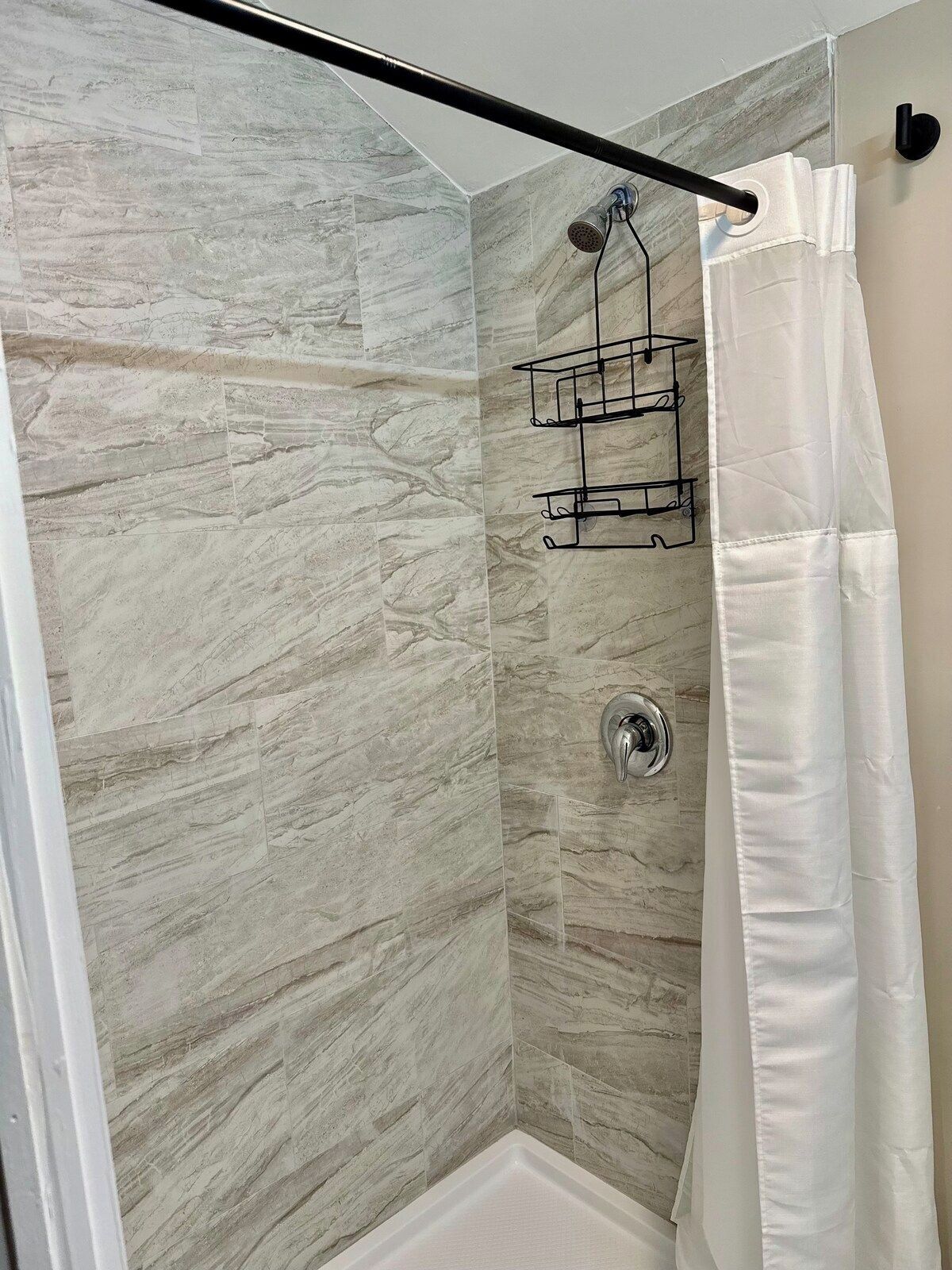 A shower area with a marble wall, a showerhead, a towel rack, and a white shower curtain.