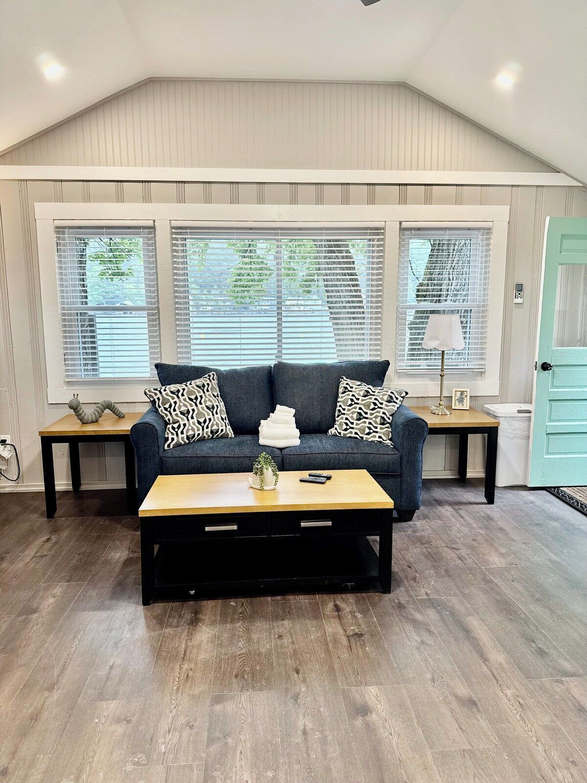 A living room with a sofa, a coffee table, and a window with blinds.