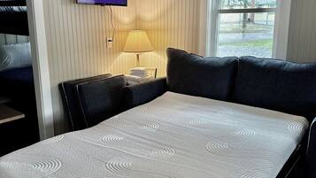 A hotel room with a bed, a television mounted on the wall, a window with a view of trees, and a lamp on a bedside table.
