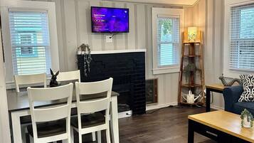 A living room with a fireplace, a television mounted on the wall, and a dining area with chairs.