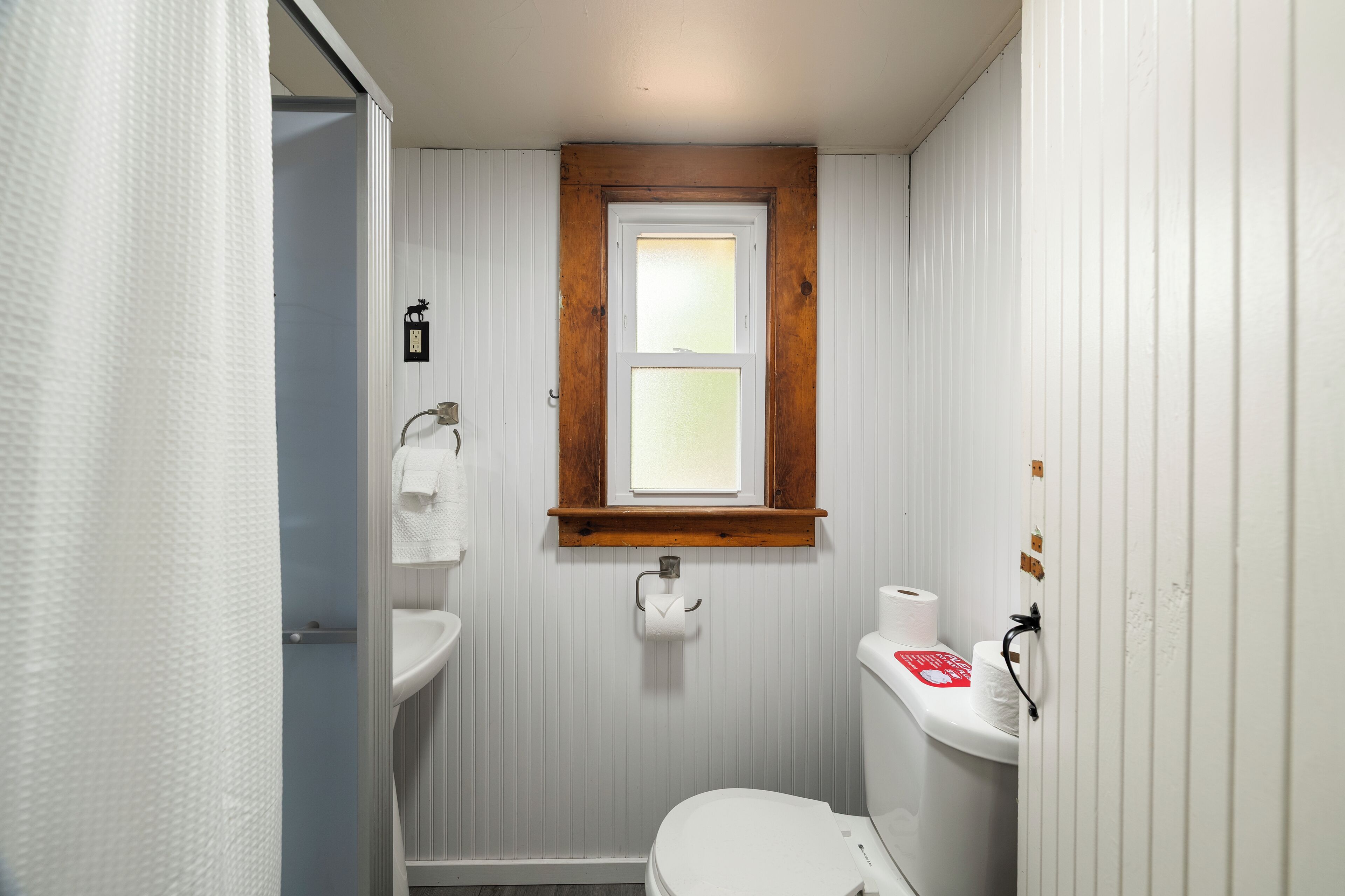 Une petite salle de bain compacte, équipée de toilettes, d’un lavabo et d’une fenêtre située au-dessus du lavabo.