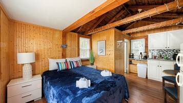 Une cabane en bois comprenant un lit, une table de chevet, une lampe, une fenêtre, un coin cuisine et une table à manger.