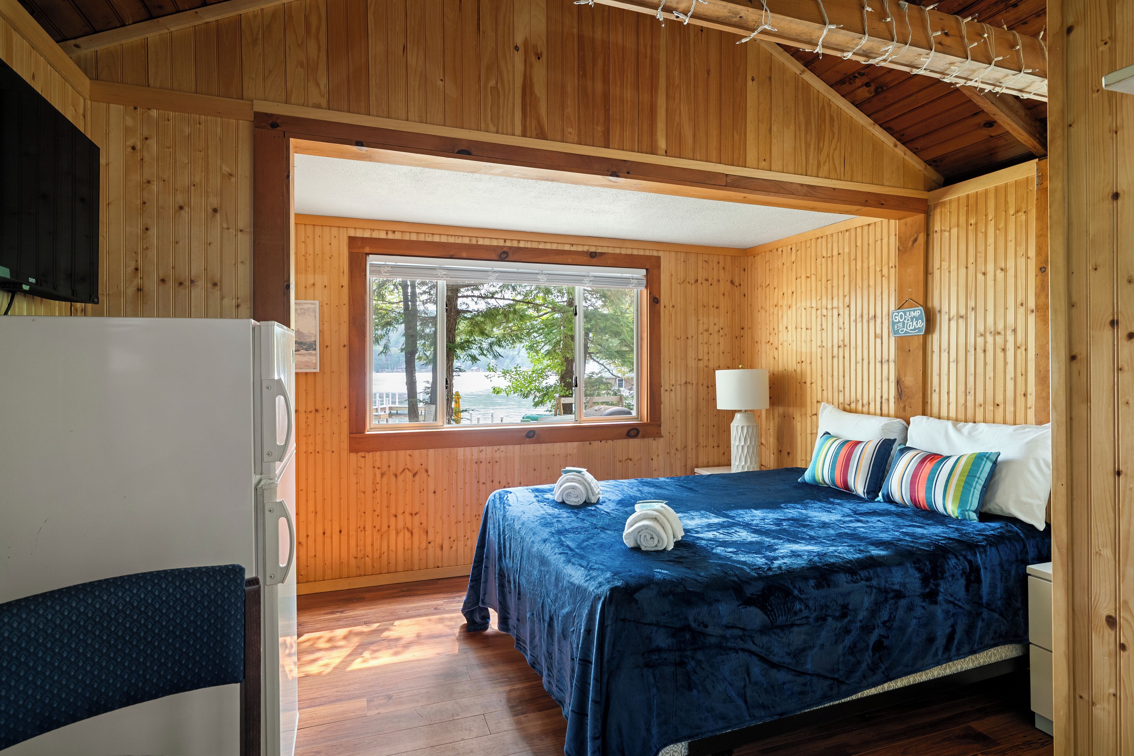 Una habitación tipo cabaña de madera con una cama, una ventana, un refrigerador y un cartel en la pared.