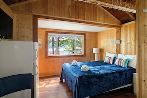 Quarto de cabana de madeira com cama, janela, geladeira e um aviso na parede.
