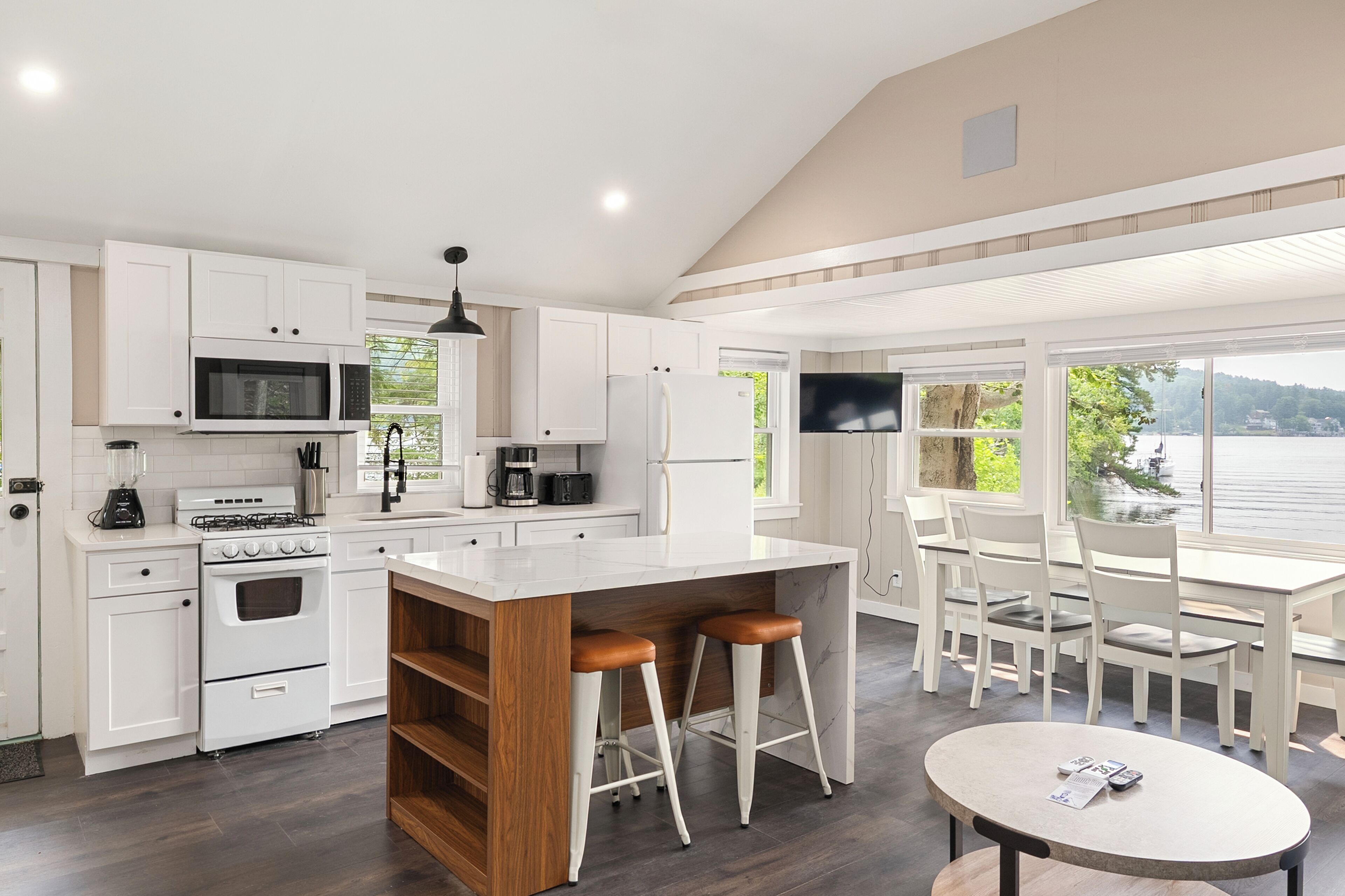 Una cocina moderna con armarios blancos, una isla central y un comedor con vista al lago.