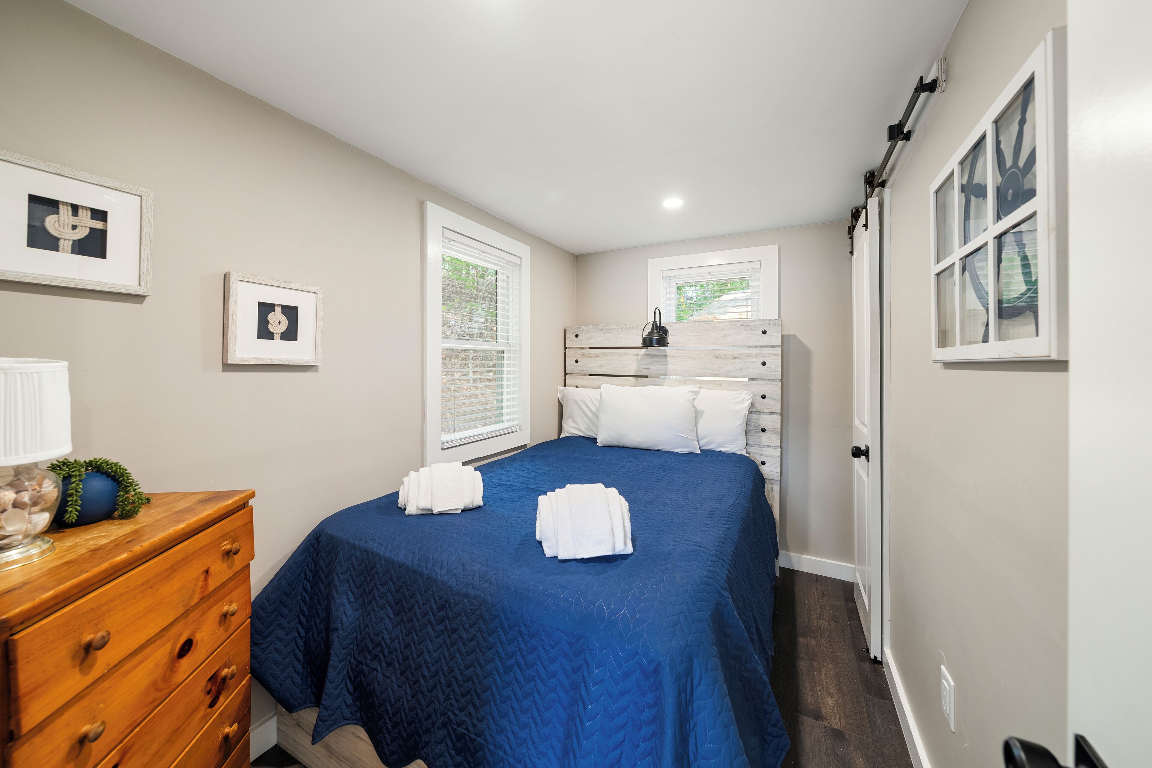 Un dormitorio con cama, cómoda y dos ventanas.