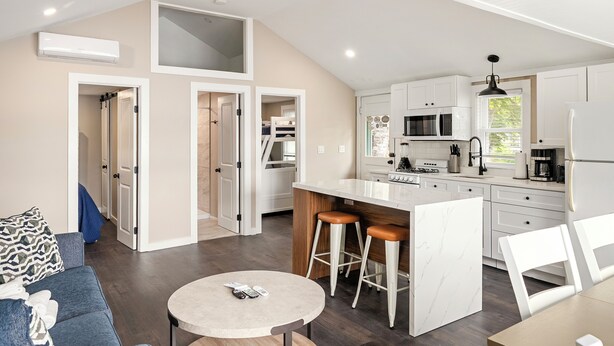 A modern kitchen with a central island, bar stools, and a dining table. - Cabin 48 at Historic Sandy Point Resort W/ Boat Slip and Onsite Boat Ramp (Alton)