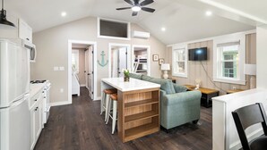A modern kitchen with a central island, a dining area with a green sofa, and a TV mounted on the wall. - Cabin 45 at Historic Sandy Point Resort W/ Boat Slip and Onsite Boat Ramp (Alton)