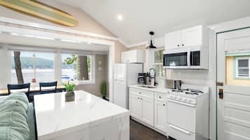 Uma cozinha moderna com armários brancos, uma ilha central e vista para o exterior.