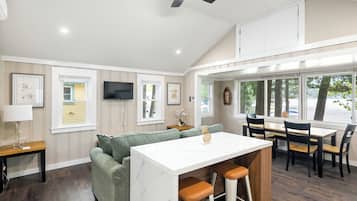 A modern kitchen with a bar area, wooden flooring, and large windows.