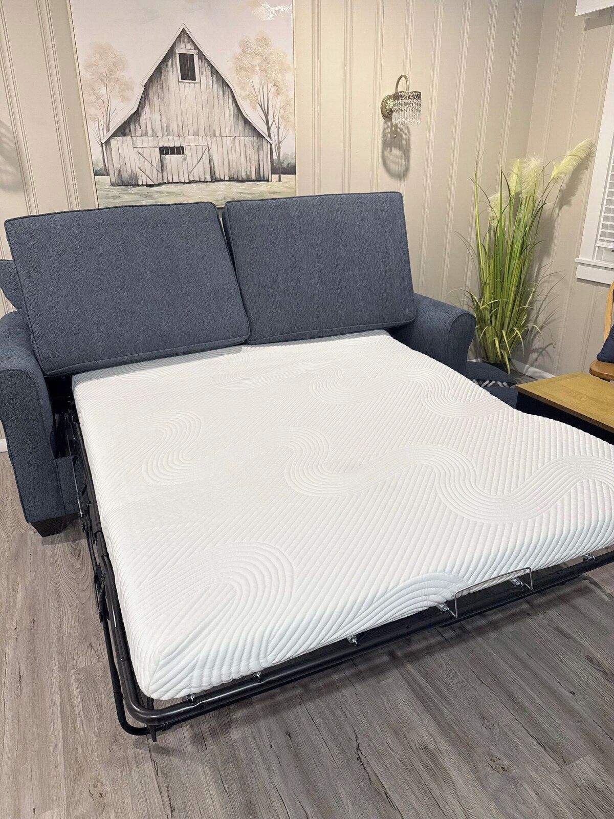 A bed with a mattress, grey upholstered headboard, and a wall-mounted light fixture.