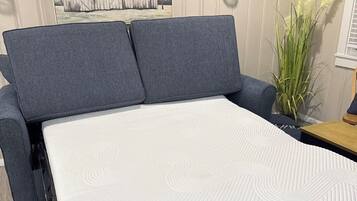 A bed with a mattress, grey upholstered headboard, and a wall-mounted light fixture.