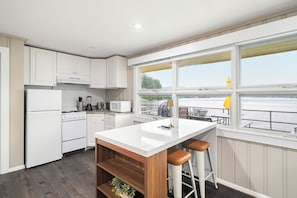 A modern kitchen with white cabinetry, a central island with stools, and a view of the water through large windows. - Cabin 32 at Historic Sandy Point Resort W/ Boat Slip and Onsite Boat Ramp (Alton)