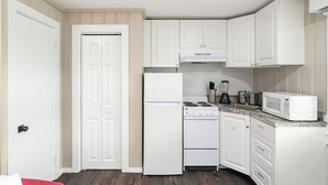 A compact kitchen with white cabinetry, a refrigerator, a stove, a microwave, and a sink.