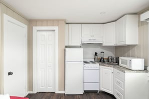 A compact kitchen with white cabinetry, a refrigerator, a stove, a microwave, and a sink.