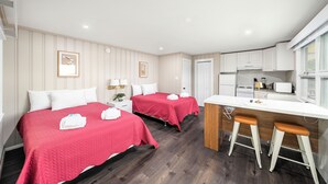A hotel room with two beds, a kitchenette, and a bathroom.