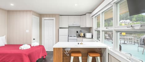 Una habitación de hotel pequeña con cama, kitchenette y vistas al exterior.