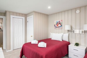 A hotel room with a bed, a nightstand, a lamp, a painting, and a door.