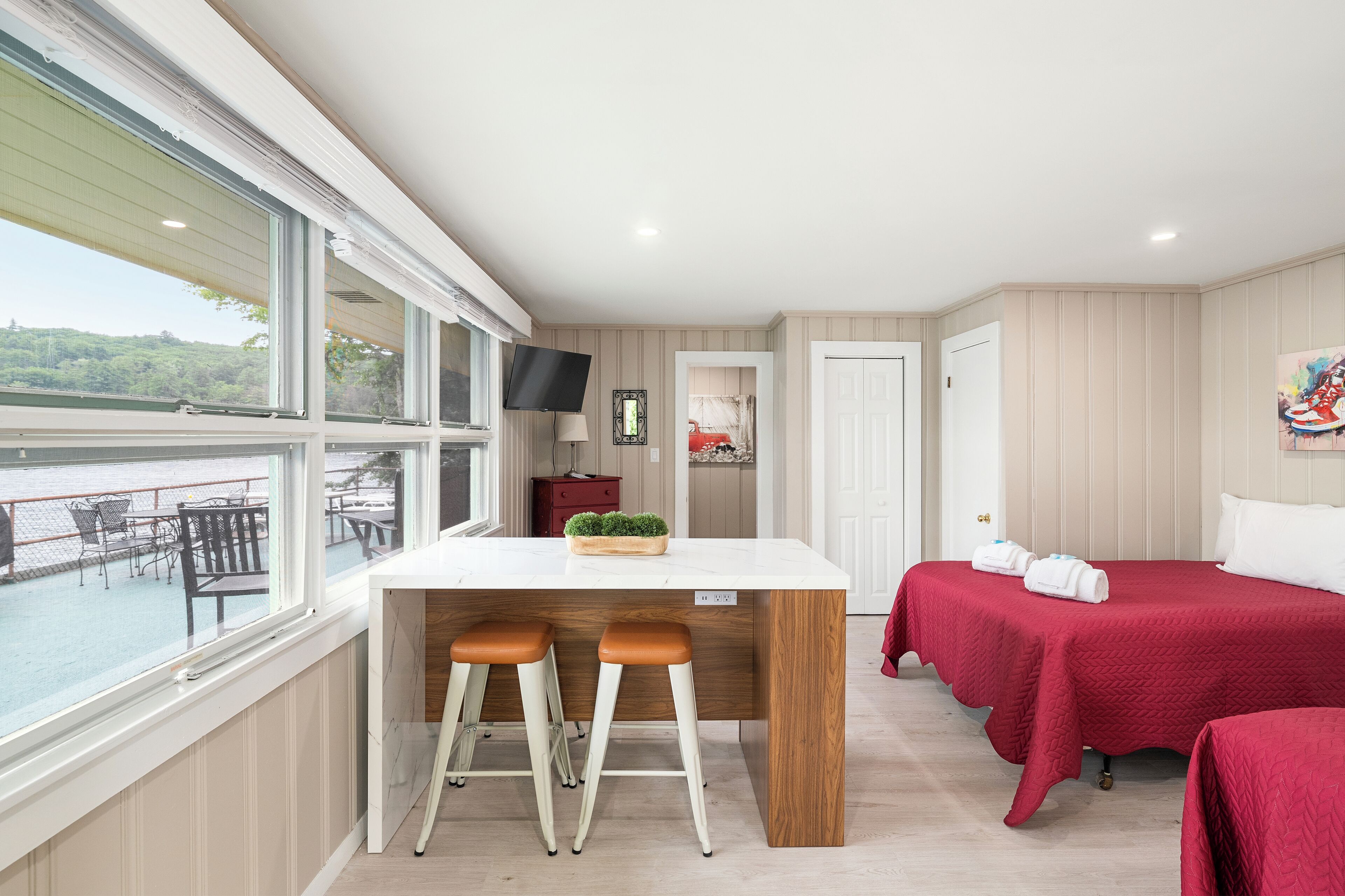 Une chambre d’hôtel avec un balcon, un lit, un bureau avec deux tabourets et un téléviseur.