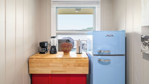 A compact kitchen with a wooden countertop, a blue refrigerator, a coffee maker, and a basket.