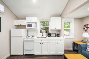 A compact kitchen with white cabinetry, a gas stove, a microwave, and a coffee maker.