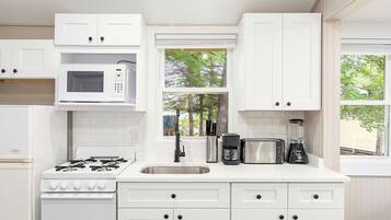 A modern kitchen with white cabinets, a microwave, a stove, a sink, and various appliances.