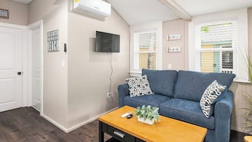 Een woonkamer met een blauwe bank, een houten salontafel, een wandtelevisie en een luchtverwarmer.