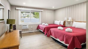 A hotel room with two beds, a desk, a chair, a window with a view, and a lamp.