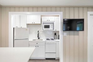 A modern kitchen with white cabinetry, a microwave, a stove, and a sink.