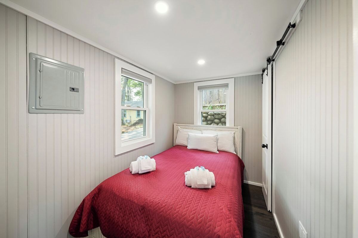 Een slaapkamer met een bed, twee ramen, een deur en een wandlamp.