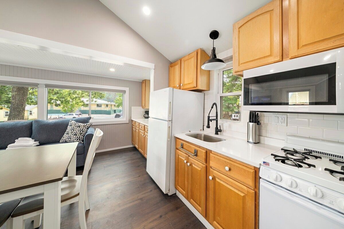 A modern kitchen with wooden cabinets, a white refrigerator, a stove, and a dining area with a table and chairs.