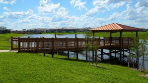 A wooden gazebo over a lake, surrounded by green grass and a row of houses in the background. - Storey Lake: Cozy 2BR Near Disney (Kissimmee)