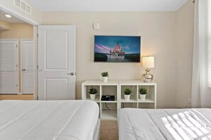 Une chambre d’hôtel avec deux lits, un téléviseur fixé au mur, un bureau avec une lampe et un tableau représentant un château.