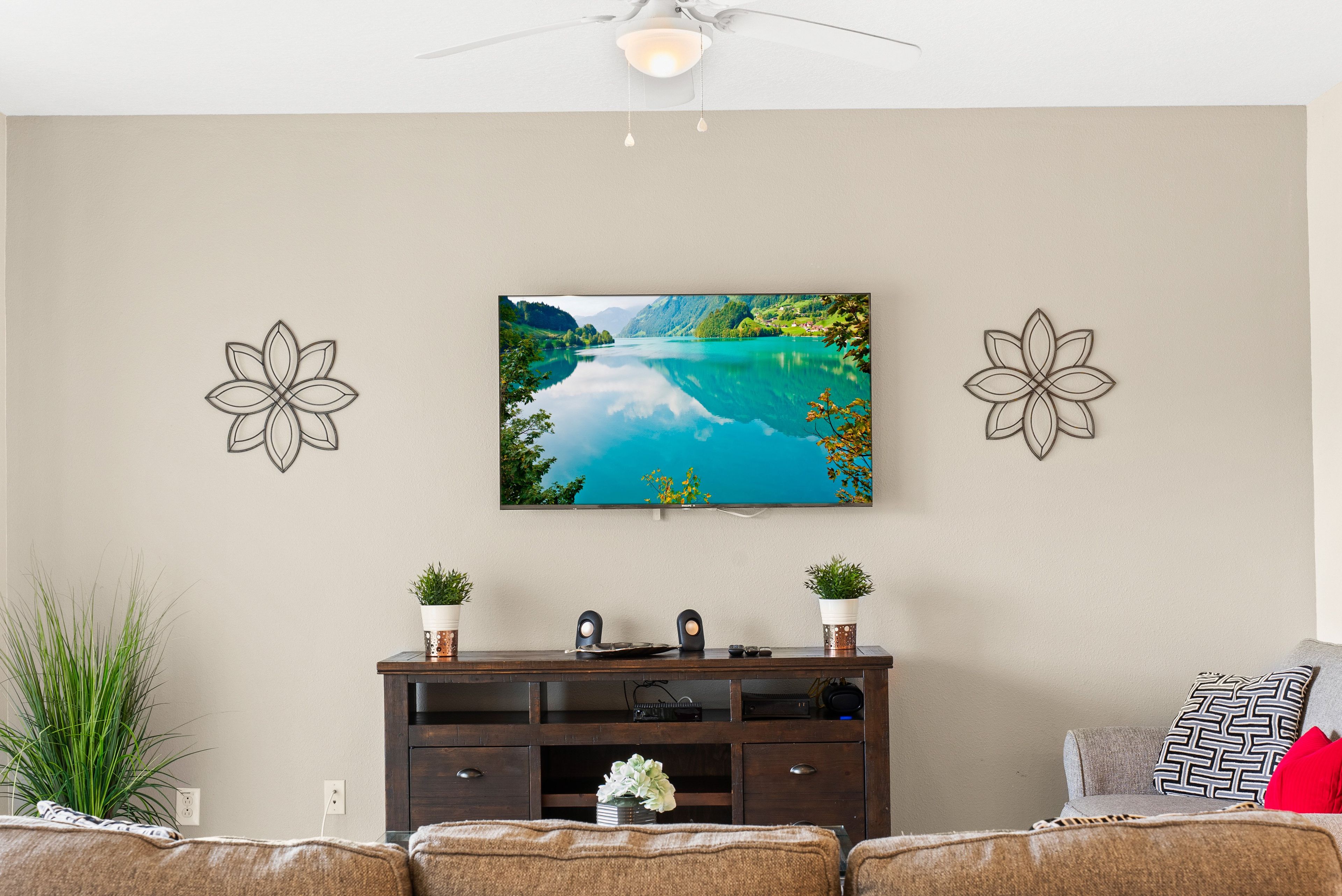 A living room with a television mounted on the wall, a dark wooden cabinet below, and two decorative wall art pieces.